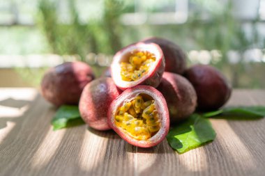 Bir grup mor derili çarkıfelek meyvesi, güneş ışığı altında kesilmiş ve yuvarlak meyveler ahşap masa üzerinde, bulanık arka plan