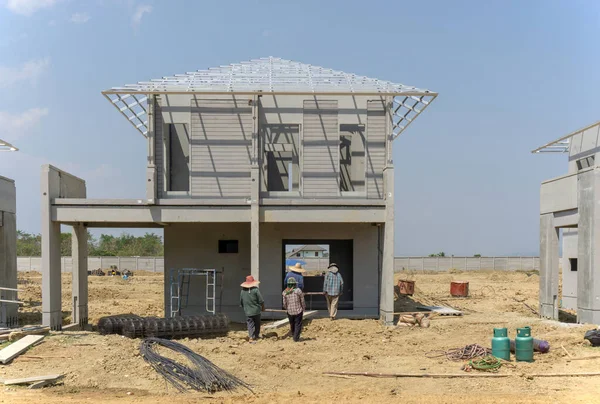 Konut inşaatı devam ediyor, insanlar precast bir ev inşa ediyorlar, işçiler bulutlu bir gökyüzünün altında evin önünde çalışıyorlar.