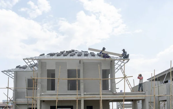 People are building a precast house on construction progress in a real estate property project site, two workman working on the roof, a worker on the terrace in a hot day under cloudy sky