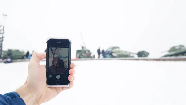 Mobile phone in hand on the background of old military equipment with reflection on the phone screen