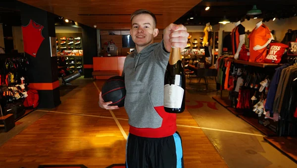 Young athletic man in sportswear with ball and wine bottle in the hand at a basketball store