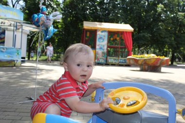 Sevimli küçük sarışın çocuk açık havada kırmızı bebek elbise yakınındaki bir araba parkında yürür