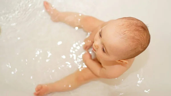 Bambino divertente che gioca con acqua e schiuma in un bagno. Bagni per bambini . — Foto Stock