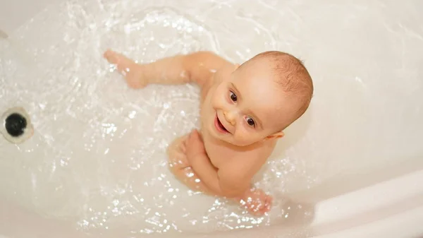 Bambino divertente che gioca con acqua e schiuma in un bagno. Bagni per bambini . — Foto Stock