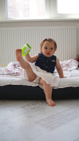Urocza Zabawna mała dziewczynka siedzi w łóżku z podniesioną nogą — Zdjęcie stockowe