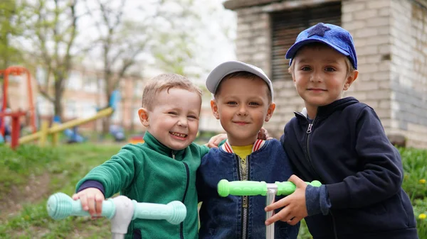 Tres adorables niños pequeños cabalgando en patinetas scooters en el patio de recreo — Foto de Stock