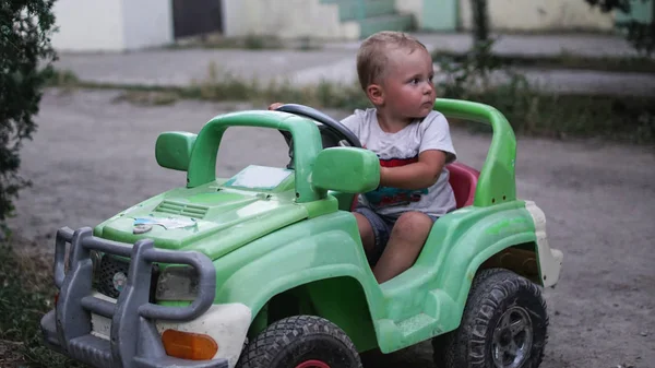 Pequeno menino pré-escolar dirigindo carro de brinquedo grande e se divertindo, ao ar livre . — Fotografia de Stock