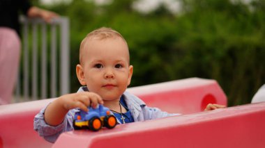 Komik küçük çocuk oyun alanında plastik gül çitler arasında oturan