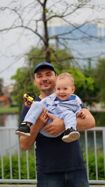 Feliz padre sosteniendo a su hijo en el brazo, caminando juntos en un parque — Foto de Stock