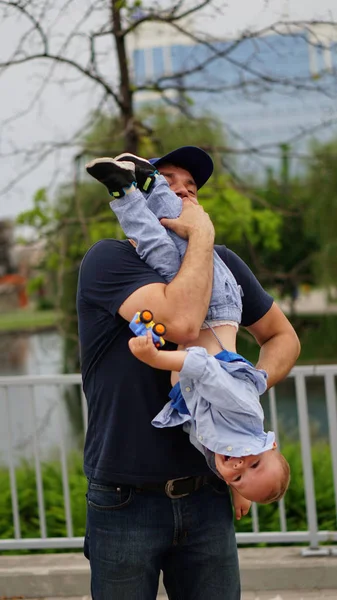 Happy dad holding his son on arm upside down, walking together in a park