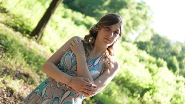 Güneşli bir günde bir parkta bukleler ile beyaz elbiseli neşeli hamile kadın