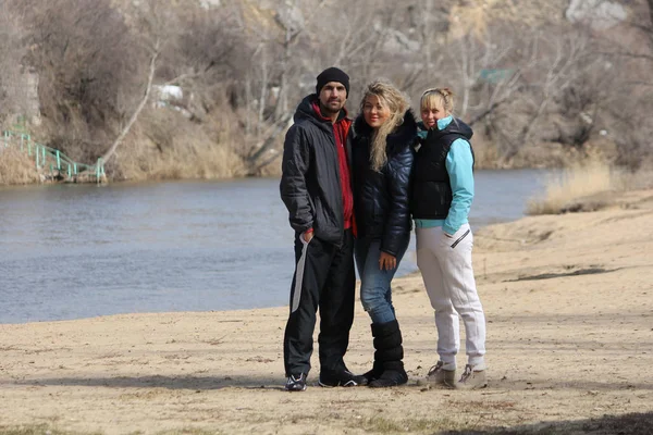 Man and two attractive women on the beach of the river in early spring