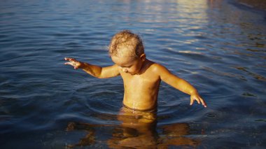 Küçük çocuk yüzmek için suya girer ve denizin dibine bakar..