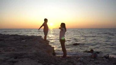 Denizde gün batımı bir arka plan karşı küçük bir çocuk ve annesinin siluetleri . Çocuk taştan annenin kollarına atlar