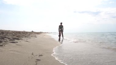 Genç ve güzel bir anne ve onun küçük oğlu deniz kıyısında yürüyüş ve dalgalar izliyor