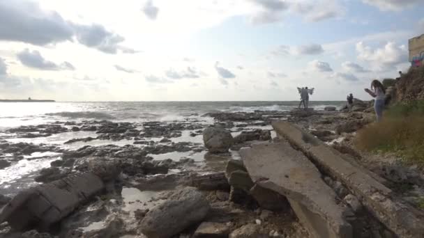 人们站在岩石上 在海上看日落 海浪在海岸上的岩石上破浪飞溅 夏天在海洋上翻滚的波浪 — 图库视频影像