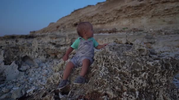 Gün Batımında Deniz Kıyısındaki Taşların Üzerinde Oturan Çocuk Çocuk Kendi — Stok video