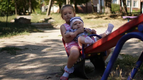 Duas meninas inteligentemente vestidas montando em um balanço no playground — Fotografia de Stock