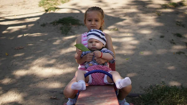 Duas meninas inteligentemente vestidas montando em um balanço no playground — Fotografia de Stock