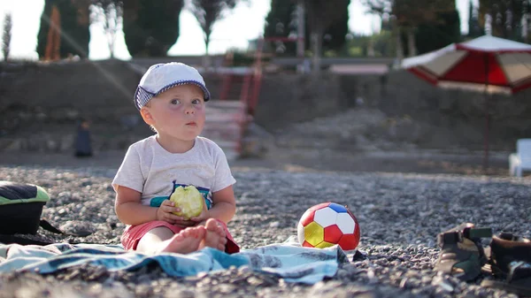 Cute dziecko siedzi na macie na plaży i jedzenia jabłko — Zdjęcie stockowe