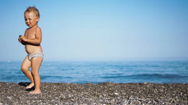 Niedliches Kind mit einem Stein am Strand. Meer im Hintergrund . — Stockfoto