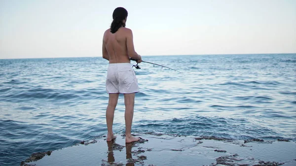 Homme adulte pêchant debout sur la jetée. Mer bleue et ciel sur le fond . — Photo