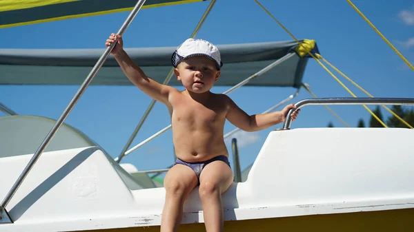 Sahilde teknede oturan şapka takan çocuk. Denizde tatilde olan çocuk — Stok fotoğraf
