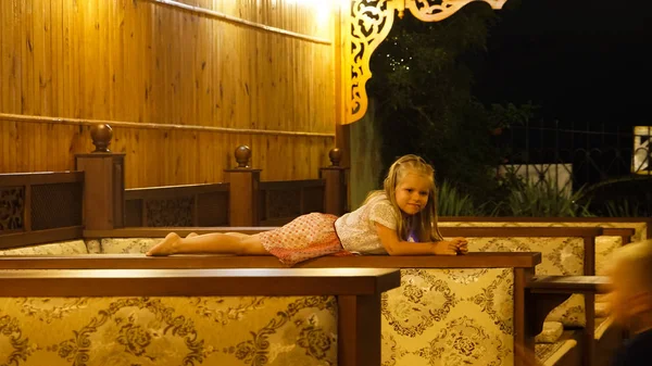 Menina bonito em um restaurante deitado no topo do sofá e olhando para longe . — Fotografia de Stock