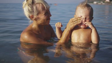 Küçük çocuk ve sarışın annesi yüzmek ve denizde oynamak için suya girer.