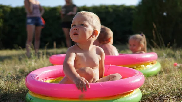 Crianças pequenas na piscina inflável no prado brincando com água — Fotografia de Stock