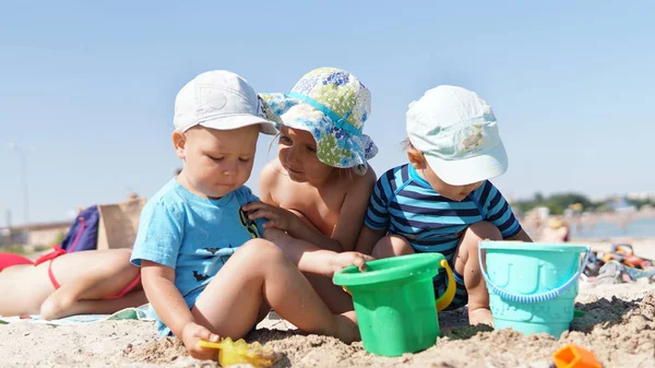 Trzy małe dzieci na plaży bawią się piaskiem — Zdjęcie stockowe