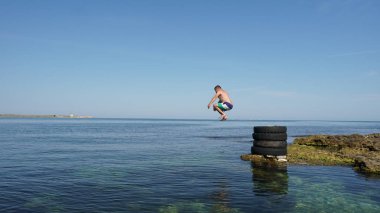 Sahildeki eski lastiklerle derin mavi denize atlayan cesur adam.