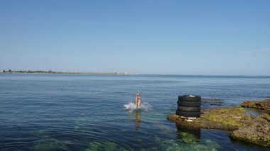 Yetenekli dalgıç sahilde eski lastiklerden derin mavi denize atlama.
