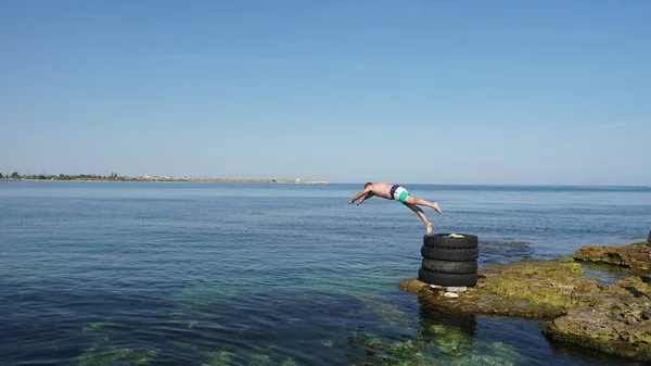 Mutiger Mann springt von alten Reifen an der Küste ins tiefblaue Meer. — Stockfoto