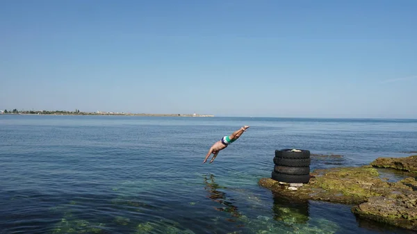 Brave man jumping to the deep blue sea from old tires on the coast.