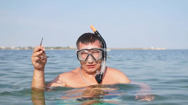 Erwachsener Mann mit Tauchermaske steht im Meer und hält einen Nadelfisch — Stockfoto