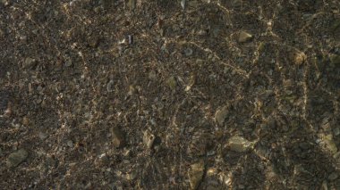 Kristal berraklığında su dalgaları ile taşlar ve kum dokusu