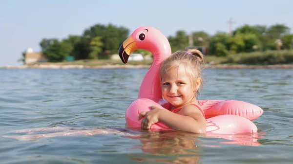Portret cute Dziewczyna uśmiechnięta pływanie z nadmuchiwane gumowe flamingi w morzu — Zdjęcie stockowe