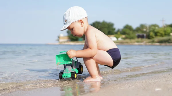 Deniz plajında oyuncak araba üzerinde çömelme sevimli küçük çocuk — Stok fotoğraf