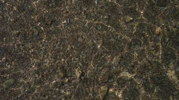 Kristal berraklığında su dalgaları ile taşlar ve kum dokusu