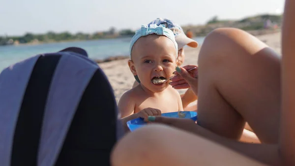 Deniz sahilinde çocuk lapası besleyen anne. Arka planda deniz kıyı şeridi — Stok fotoğraf