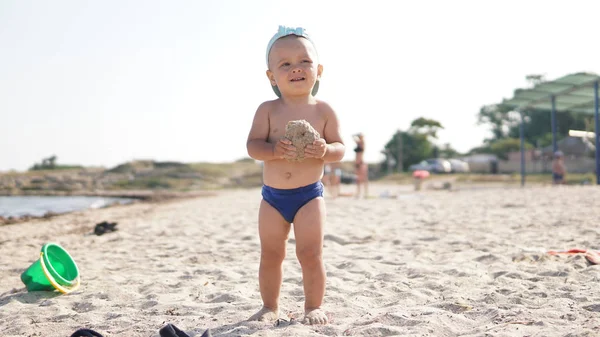 Criança em pé na praia do mar e segurando pedaço de areia molhada em sua mão . — Fotografia de Stock