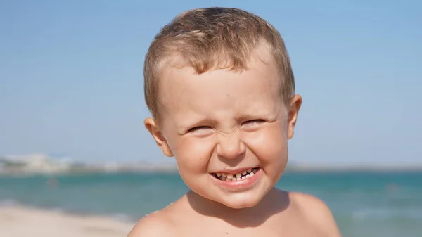Primer plano retrato de niño entrecerrando los ojos con el pelo rubio en la playa de mar — Foto de Stock