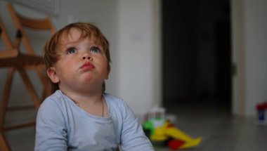 Sevimli küçük bebek kız katta oturan ve yukarı bakıyor.