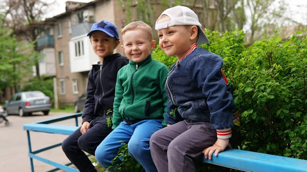 Três crianças pequenas bonitos sentados na cerca no parque infantil — Fotografia de Stock