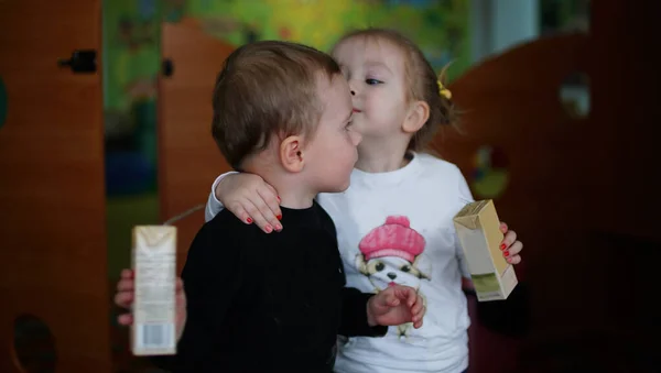 Vicces kisfiú és lány együtt isznak gyümölcslevet az óvodában. — Stock Fotó