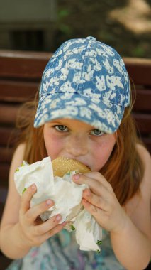 Küçük bir kızın portresi. Parkta hamburger yiyen bir çocuk.