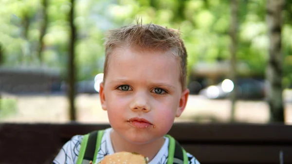 Porträtt av en liten pojke. Ett barn som äter hamburgare i parken — Stockfoto