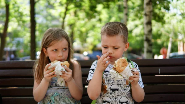 Porträtt av en liten pojke och flicka. Ett barn som äter hamburgare i parken — Stockfoto