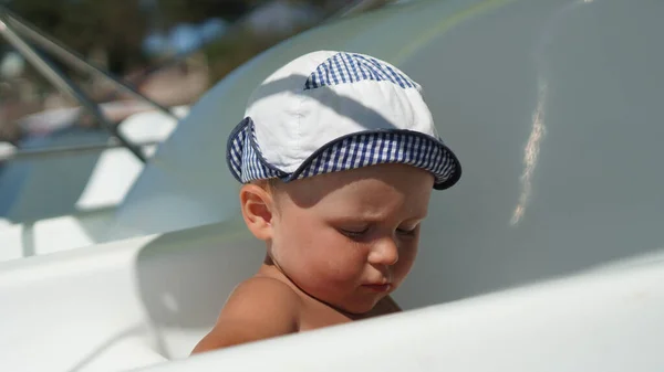 Chłopiec Biało Niebieskim Kapeluszu Siedzący Plaży Białej Łodzi Dziecko Wakacjach — Zdjęcie stockowe